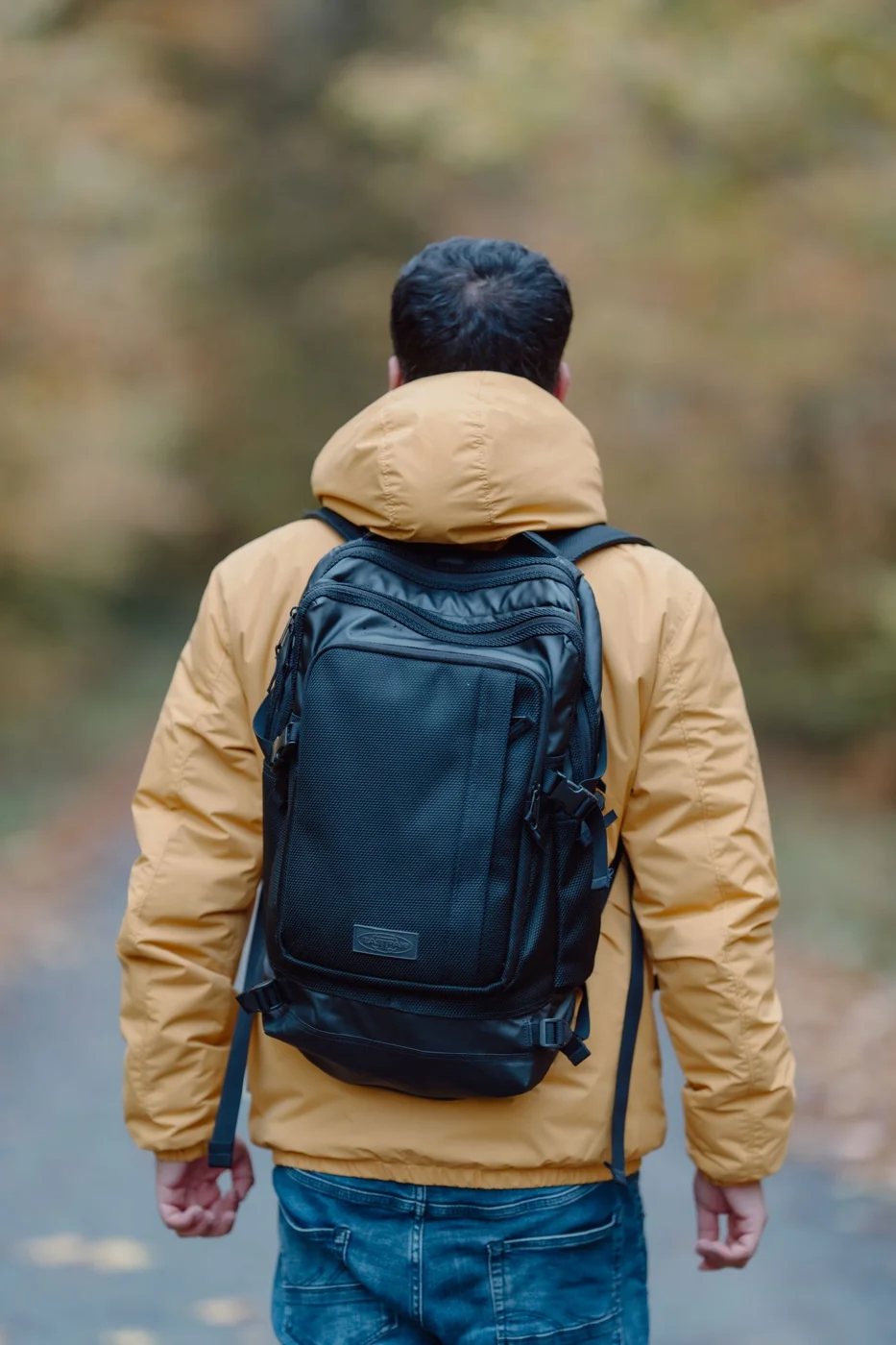 A walker wearing an outer jacket and backpack on a wooded path
